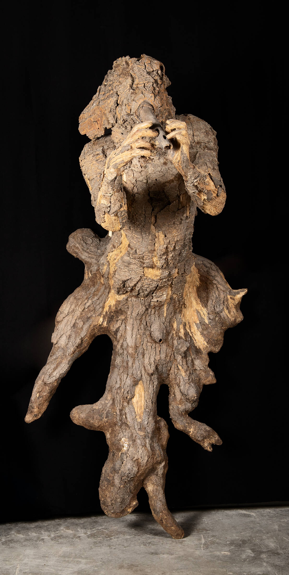 Male figure made of wood and bark playing a wind instrument.